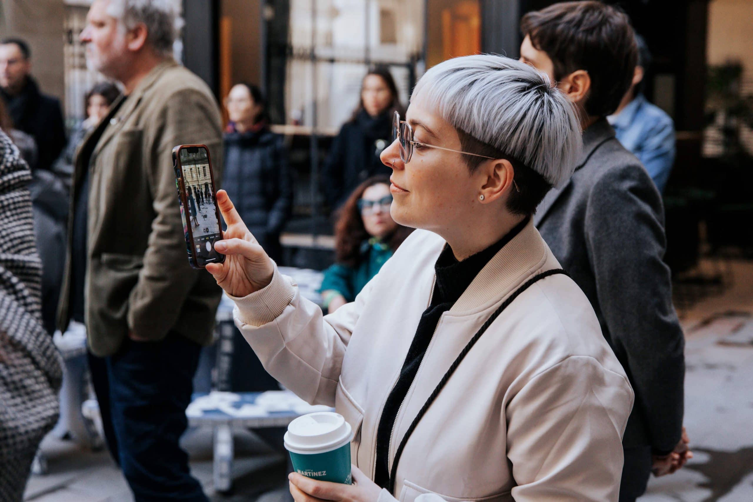 women taking a photo with cellphone coffe in hand